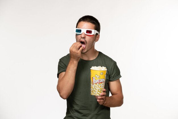 Vue de face jeune homme en t-shirt vert holding pop-corn manger dans des lunettes de soleil sur mur blanc film cinéma solitaire films masculins