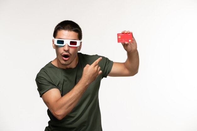 Vue de face jeune homme en t-shirt vert tenant une carte bancaire dans des lunettes de soleil sur bureau blanc films de cinéma solitaire