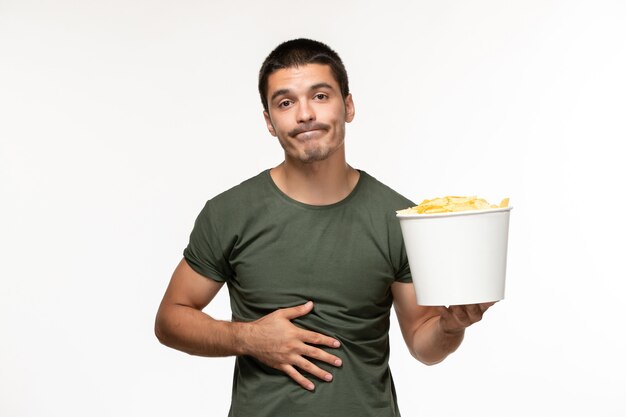 Vue de face jeune homme en t-shirt vert tenant des cips de pomme de terre sur un bureau blanc seul film film cinéma personne