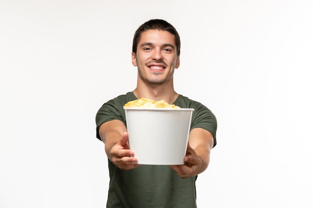 Vue de face jeune homme en t-shirt vert tenant des cips de pomme de terre sur mur blanc film seul film cinéma personne