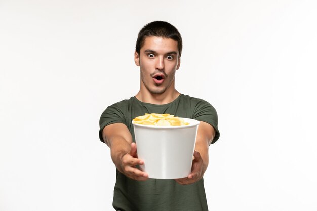 Vue de face jeune homme en t-shirt vert tenant des cips de pomme de terre sur mur blanc film seul film cinéma personne