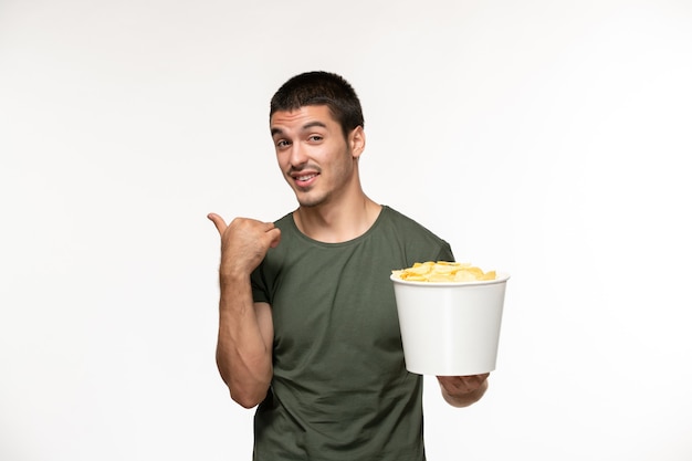 Vue de face jeune homme en t-shirt vert tenant des cips de pommes de terre sur mur blanc films de cinéma solitaire cinéma personne