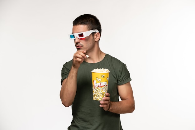 Vue de face jeune homme en t-shirt vert tenant du pop-corn dans des lunettes de soleil sur le mur blanc-clair film cinéma solitaire mâle film