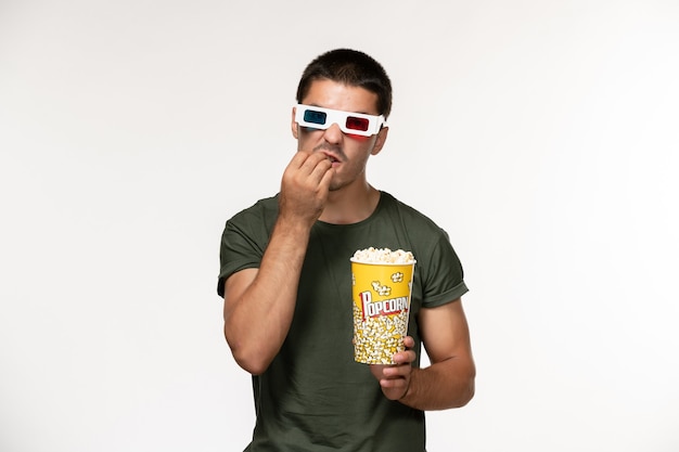 Vue de face jeune homme en t-shirt vert tenant du pop-corn dans des lunettes de soleil sur mur blanc film cinéma solitaire films masculins