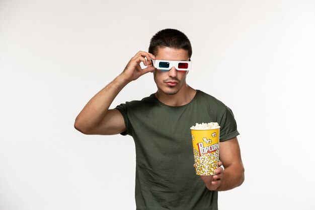 Vue de face jeune homme en t-shirt vert tenant du pop-corn dans des lunettes de soleil en regardant un film sur un bureau blanc film cinéma solitaire films masculins