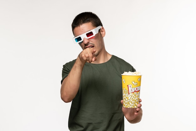 Vue de face jeune homme en t-shirt vert tenant du pop-corn dans des lunettes de soleil en regardant un film sur mur blanc film cinéma solitaire