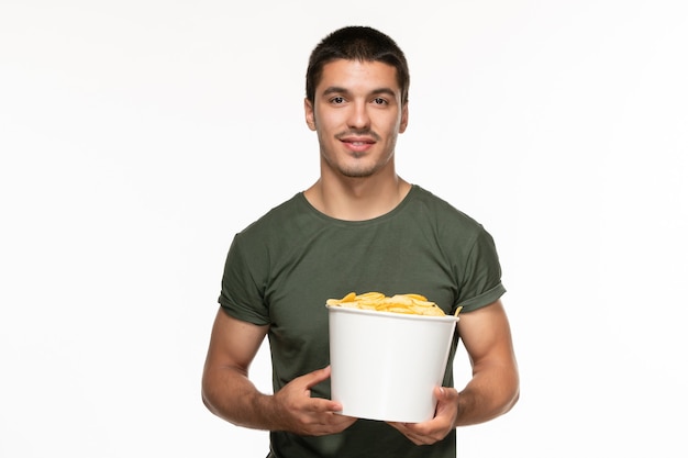 Vue de face jeune homme en t-shirt vert tenant le panier avec des cips de pommes de terre sur fond blanc cinéma film plaisir solitaire
