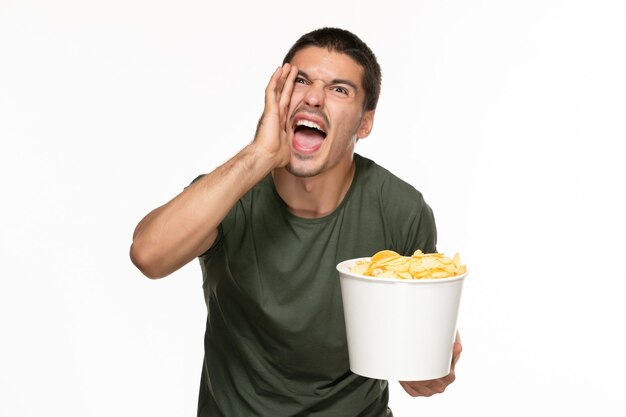 Vue de face jeune homme en t-shirt vert tenant panier avec pommes de terre cips et crier sur mur blanc cinéma de film de jouissance solitaire