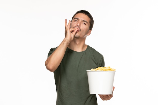 Vue de face jeune homme en t-shirt vert tenant panier avec pommes de terre cips sur mur blanc cinéma films de plaisir solitaire