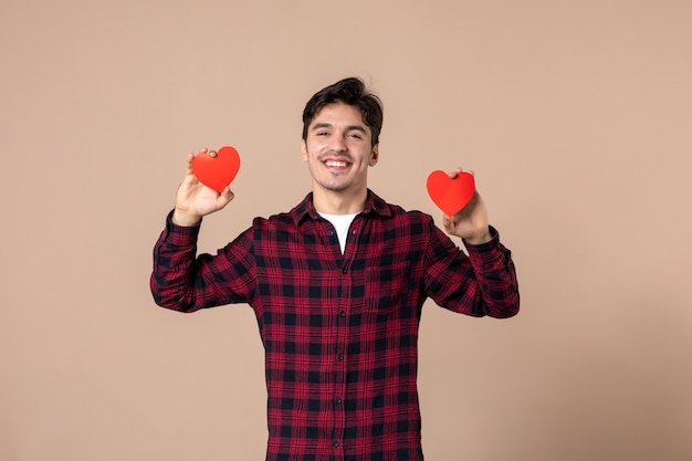 Vue de face jeune homme tenant des autocollants coeur rouge sur mur marron