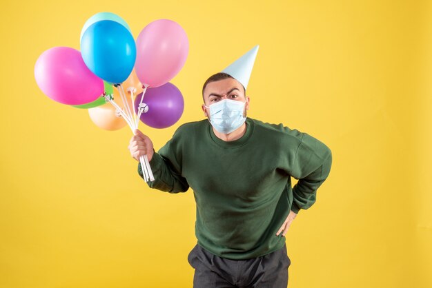 Vue de face jeune homme tenant des ballons colorés sur fond jaune