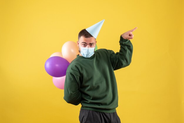 Vue de face jeune homme tenant des ballons colorés sur fond jaune