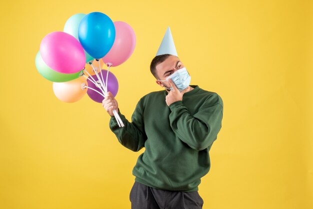 Vue de face jeune homme tenant des ballons colorés sur fond jaune