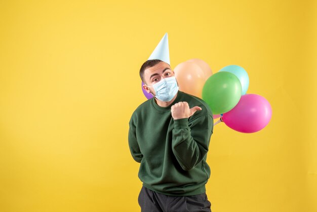 Vue de face jeune homme tenant des ballons colorés sur fond jaune