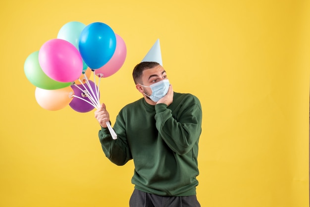 Vue de face jeune homme tenant des ballons colorés sur fond jaune