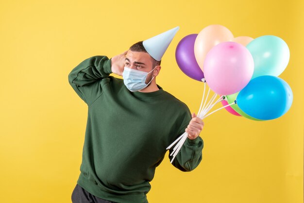 Vue de face jeune homme tenant des ballons colorés sur fond jaune