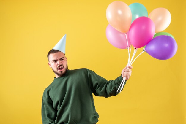 Vue de face jeune homme tenant des ballons colorés sur fond jaune