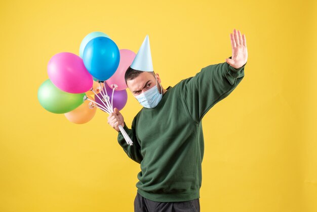 Vue de face jeune homme tenant des ballons colorés sur fond jaune