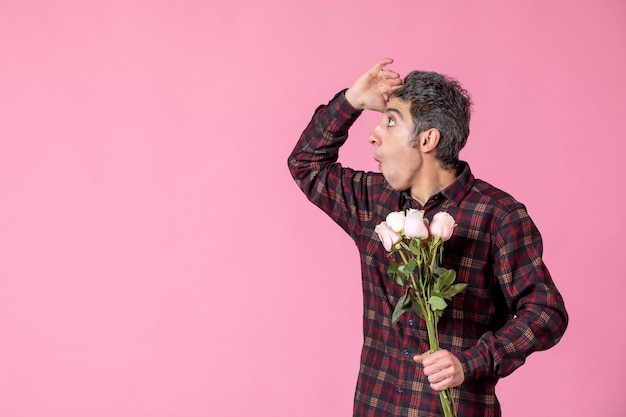 Vue de face jeune homme tenant de belles roses roses sur un mur rose