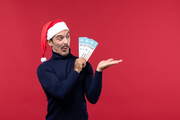 Vue de face jeune homme tenant des billets d'avion sur un bureau rouge