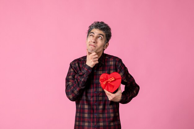 Vue De Face Jeune Homme Tenant Un Cadeau En Forme De Coeur Rouge Sur Un Mur Rose Photo gratuit