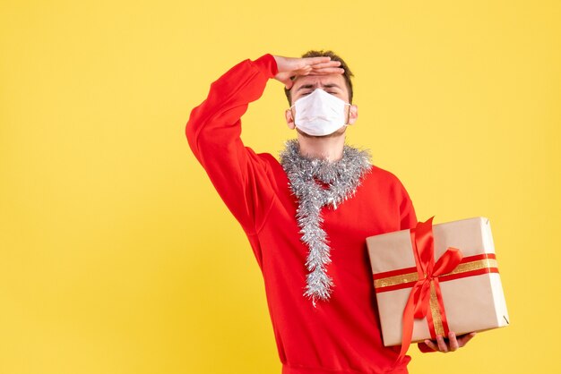Vue de face jeune homme tenant un cadeau de Noël dans un masque stérile