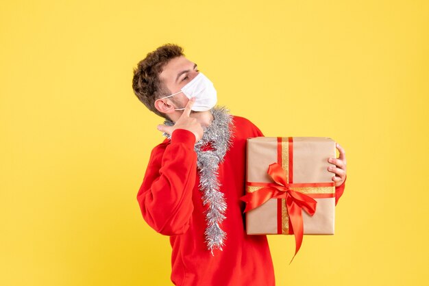 Vue de face jeune homme tenant un cadeau de Noël dans un masque stérile