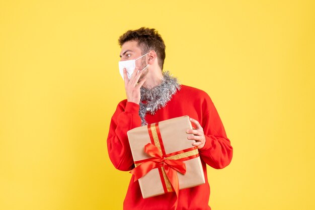 Vue de face jeune homme tenant un cadeau de Noël dans un masque stérile