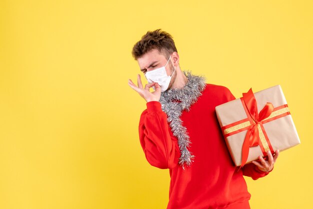 Vue de face jeune homme tenant un cadeau de Noël en masque