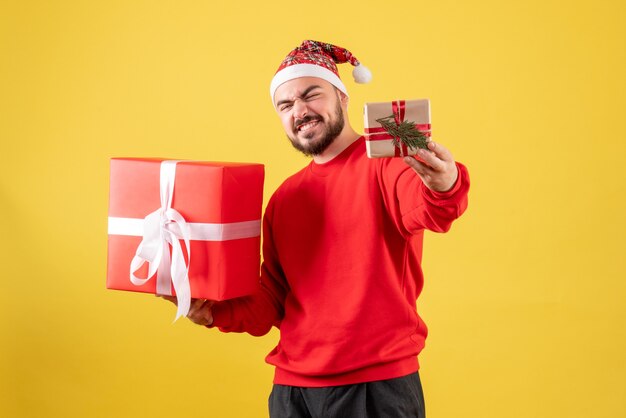 Vue de face jeune homme tenant des cadeaux de Noël sur fond jaune