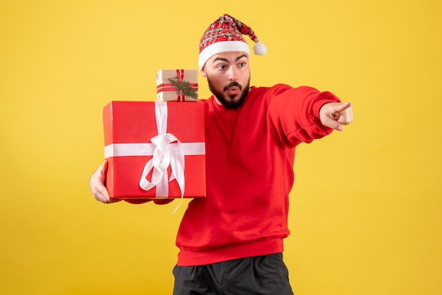 Vue de face jeune homme tenant des cadeaux de Noël sur fond jaune