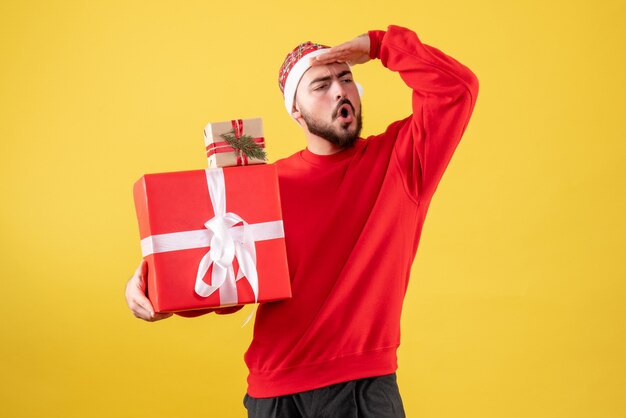 Vue de face jeune homme tenant des cadeaux de Noël sur jaune