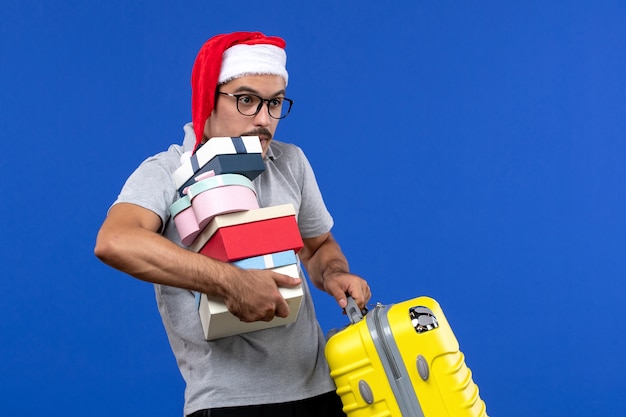 Vue de face jeune homme tenant des cadeaux et un sac sur des vacances de vol avion fond bleu