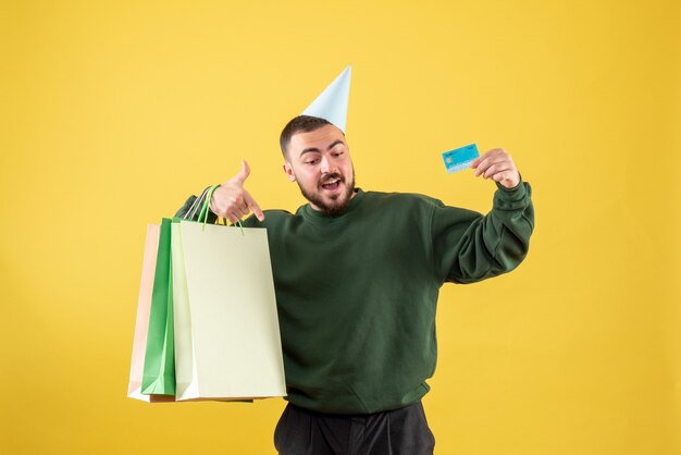 Vue de face jeune homme tenant une carte bancaire et des paquets d'achat sur fond jaune