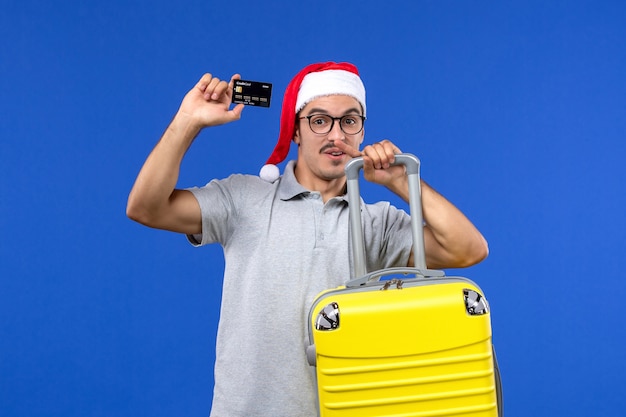 Vue de face jeune homme tenant une carte bancaire sac jaune sur les vols d'avion de vacances mur bleu