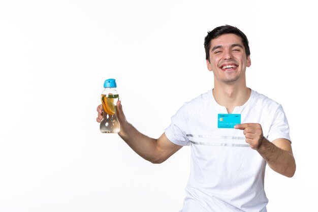 Vue de face jeune homme tenant une carte de crédit bleue et une bouteille de limonade sur fond blanc jus de peau argent soda aux fruits glacé frais