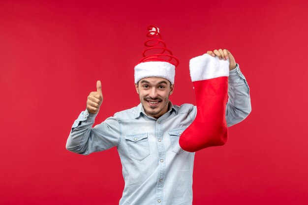 Vue de face jeune homme tenant une chaussette de noël sur un bureau rouge vacances noël