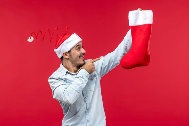 Vue de face jeune homme tenant la chaussette de Noël, Noël de vacances