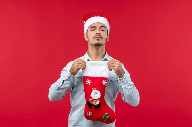 Vue de face jeune homme tenant une chaussette de noël sur un sol rouge vacances noël