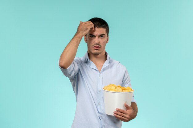 Vue de face jeune homme tenant des cips de pommes de terre sur un bureau bleu lonely remote male movie cinema
