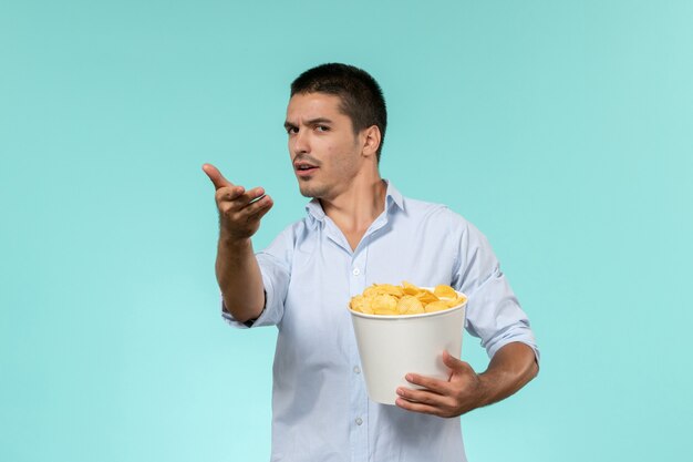 Vue de face jeune homme tenant des cips de pommes de terre sur le mur bleu cinéma films à distance solitaire