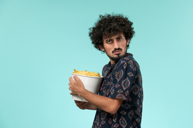 Vue de face jeune homme tenant des cips de pommes de terre sur le mur bleu clair mâle cinéma cinéma cinéma