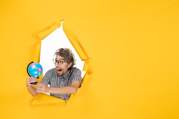 Vue de face jeune homme tenant un globe terrestre sur fond jaune monde pays émotion couleur de Noël planète vacances