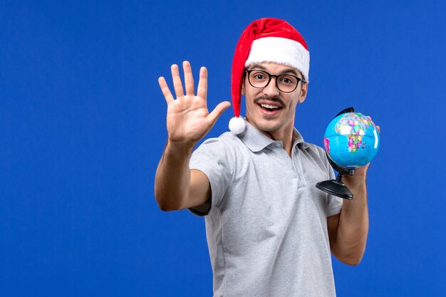 Vue de face jeune homme tenant le globe terrestre sur le mur bleu avion vacances mâle