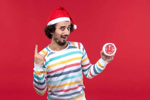 Vue de face jeune homme tenant heureusement des horloges sur le mur rouge vacances nouvel an mâle rouge
