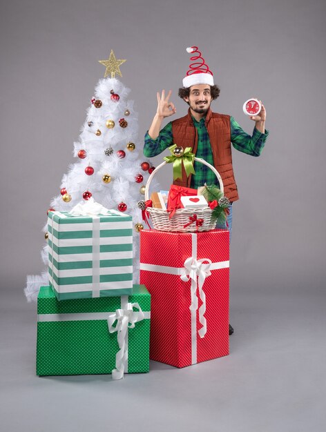 Vue de face jeune homme tenant une horloge autour de cadeaux sur un bureau lumineux cadeau noël nouvel an