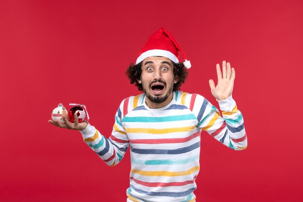 Vue de face jeune homme tenant des jouets d'arbre de Noël sur mur rouge nouvel an vacances humaines rouge