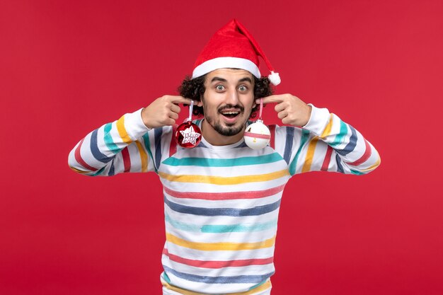 Vue de face jeune homme tenant des jouets d'arbre de Noël sur le mur rouge nouvel an vacances rouge mâle