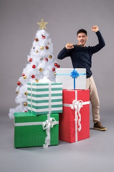 Vue de face jeune homme tenant un micro avec des cadeaux sur le gris