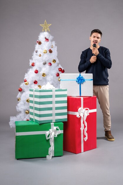 Vue de face jeune homme tenant un micro avec des cadeaux sur le gris